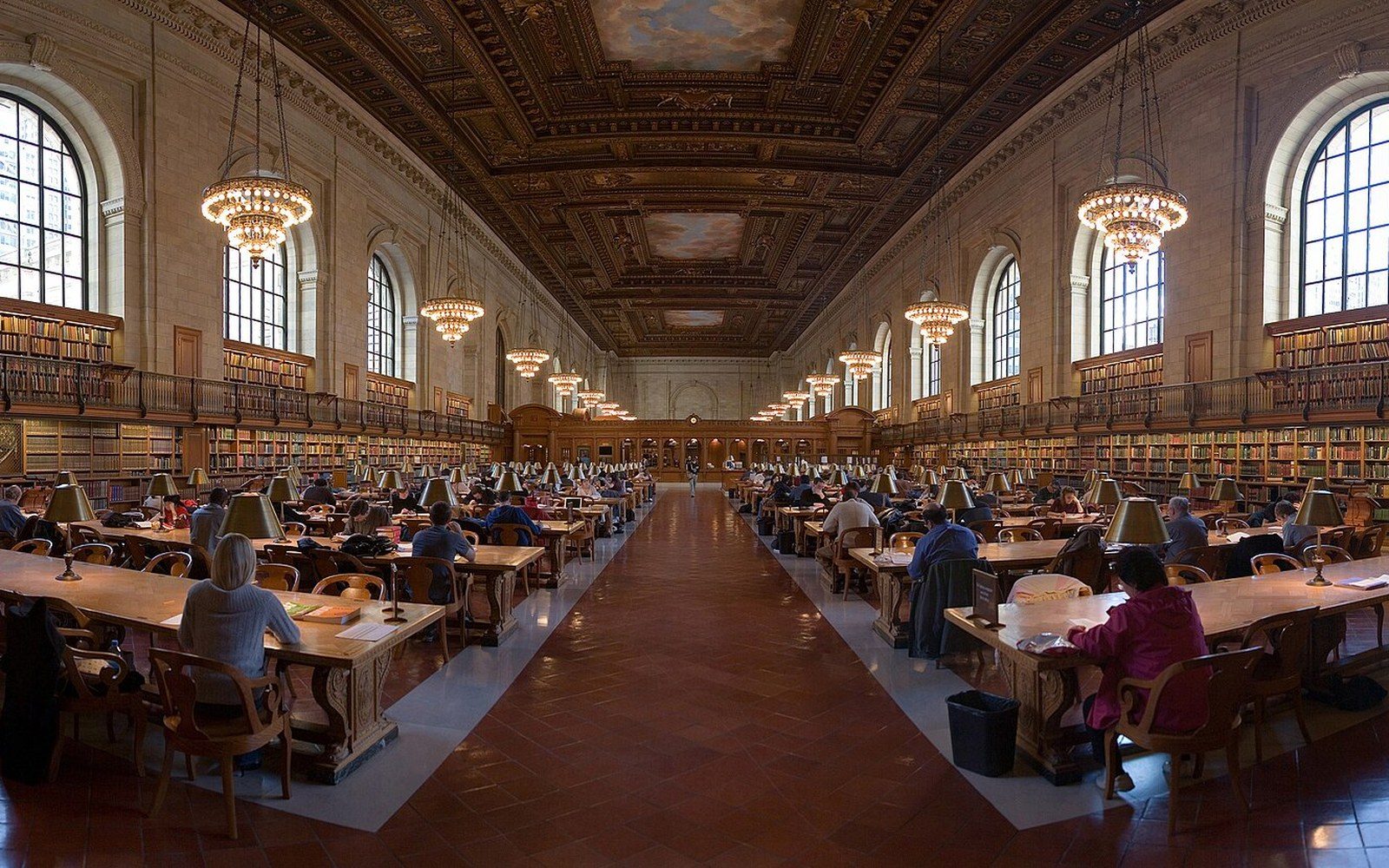 A reading-room table seen along its length, bound volumes open on cradles